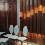 Three-dimensional blocked hardwood feature wall with warm concealed lighting beside carved double doors